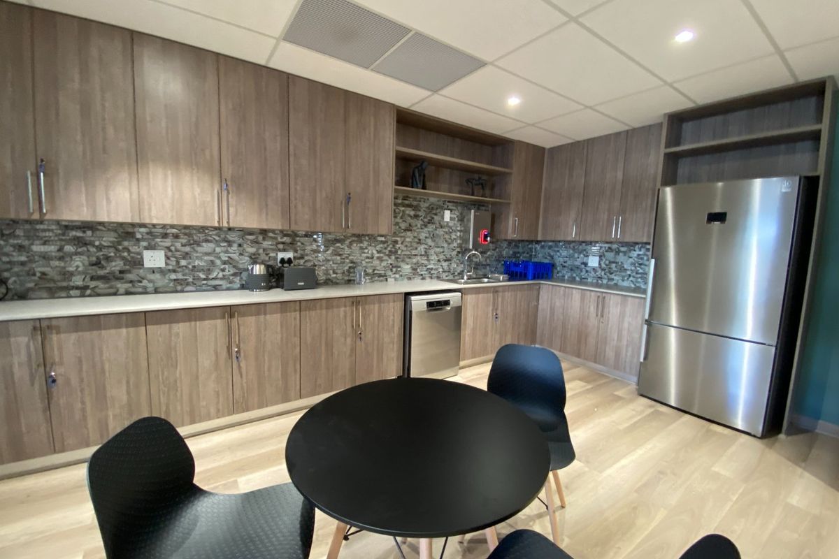 A modern commercial kitchen featuring wood-finish cabinetry, stone countertops, a mosaic tile backsplash, and integrated stainless steel appliances.