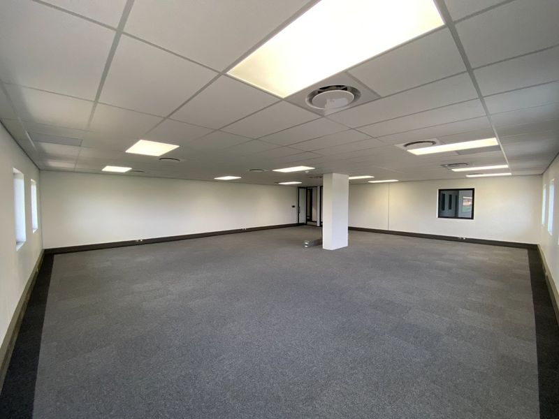 A spacious, open-plan commercial office area featuring a suspended ceiling, recessed lighting, and neutral carpet tiles, ready for custom fit-out.