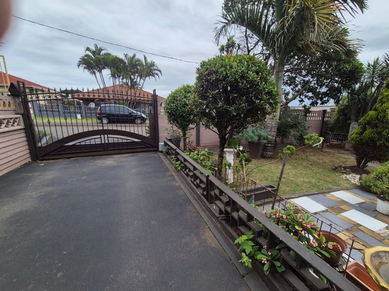 Front entrance area featuring a secure metal driveway gate, paved driveway, and established garden landscaping.