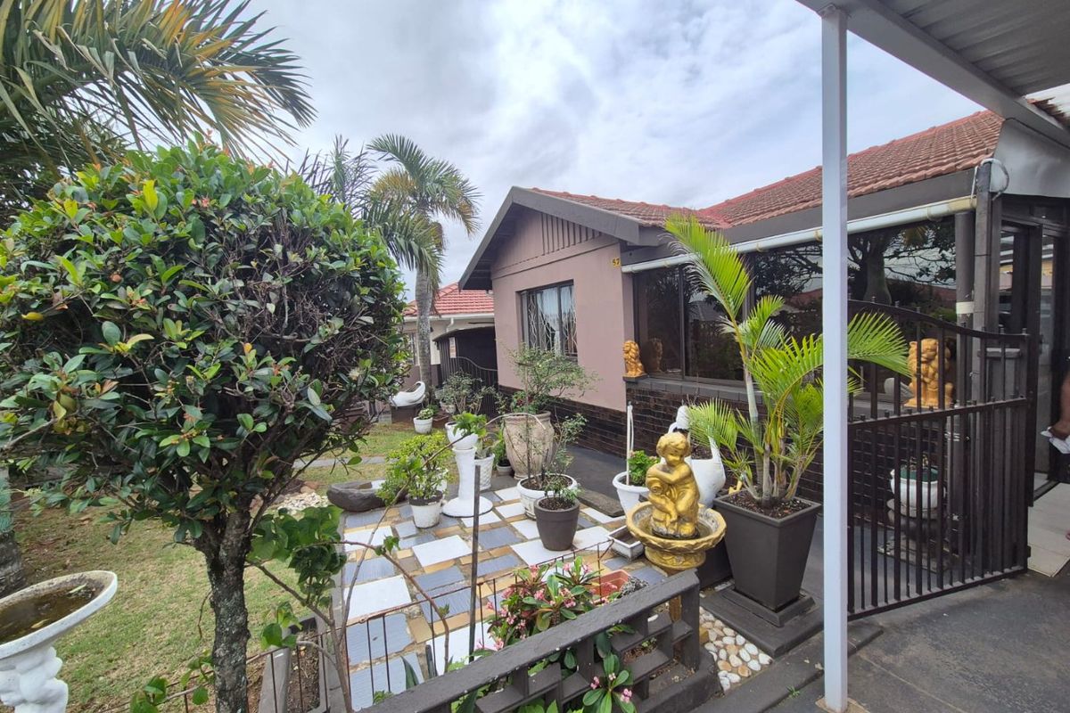 A rear exterior view of the property featuring a tiled patio area, covered walkway, and established garden landscaping.