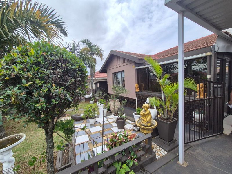 A rear exterior view of the property featuring a tiled patio area, covered walkway, and established garden landscaping.