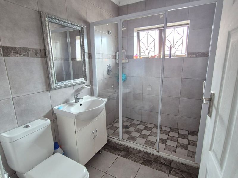 A functional bathroom featuring a vanity basin, toilet, and a glass-enclosed shower with neutral wall and floor tiling.