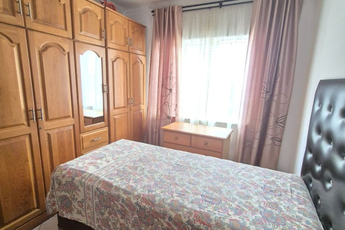 A bedroom featuring built-in wooden wardrobes and tiled flooring, offering functional storage space and natural light.