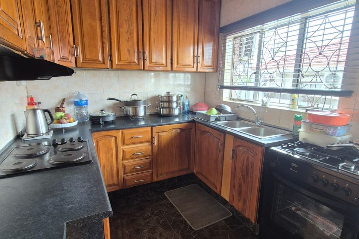A functional kitchen featuring wooden cabinetry, dark laminate countertops, a double sink, and a freestanding oven with an extractor fan.