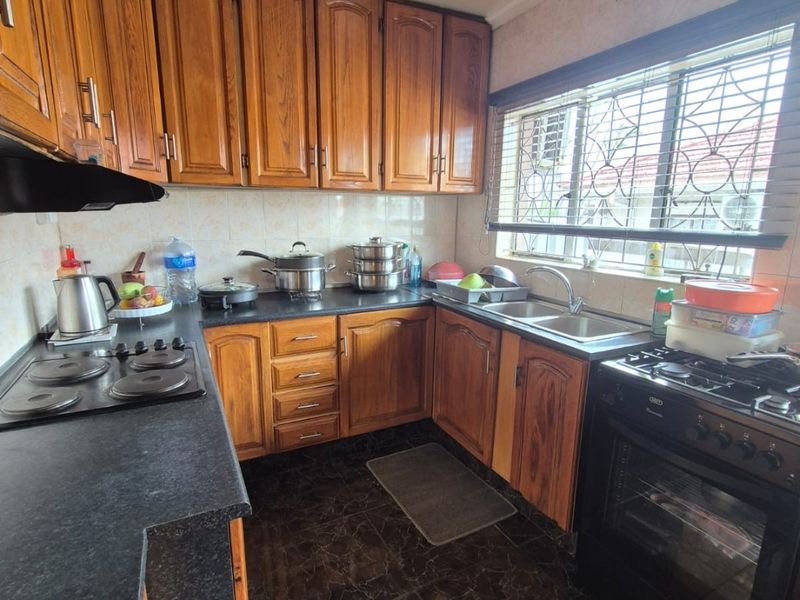A functional kitchen featuring wooden cabinetry, dark laminate countertops, a double sink, and a freestanding oven with an extractor fan.