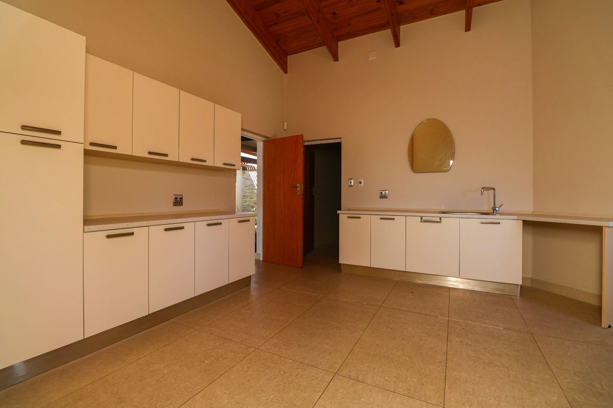 A clean, empty kitchen featuring white built-in cabinetry, laminate countertops, a stainless steel sink, and high ceilings with exposed timber beams.