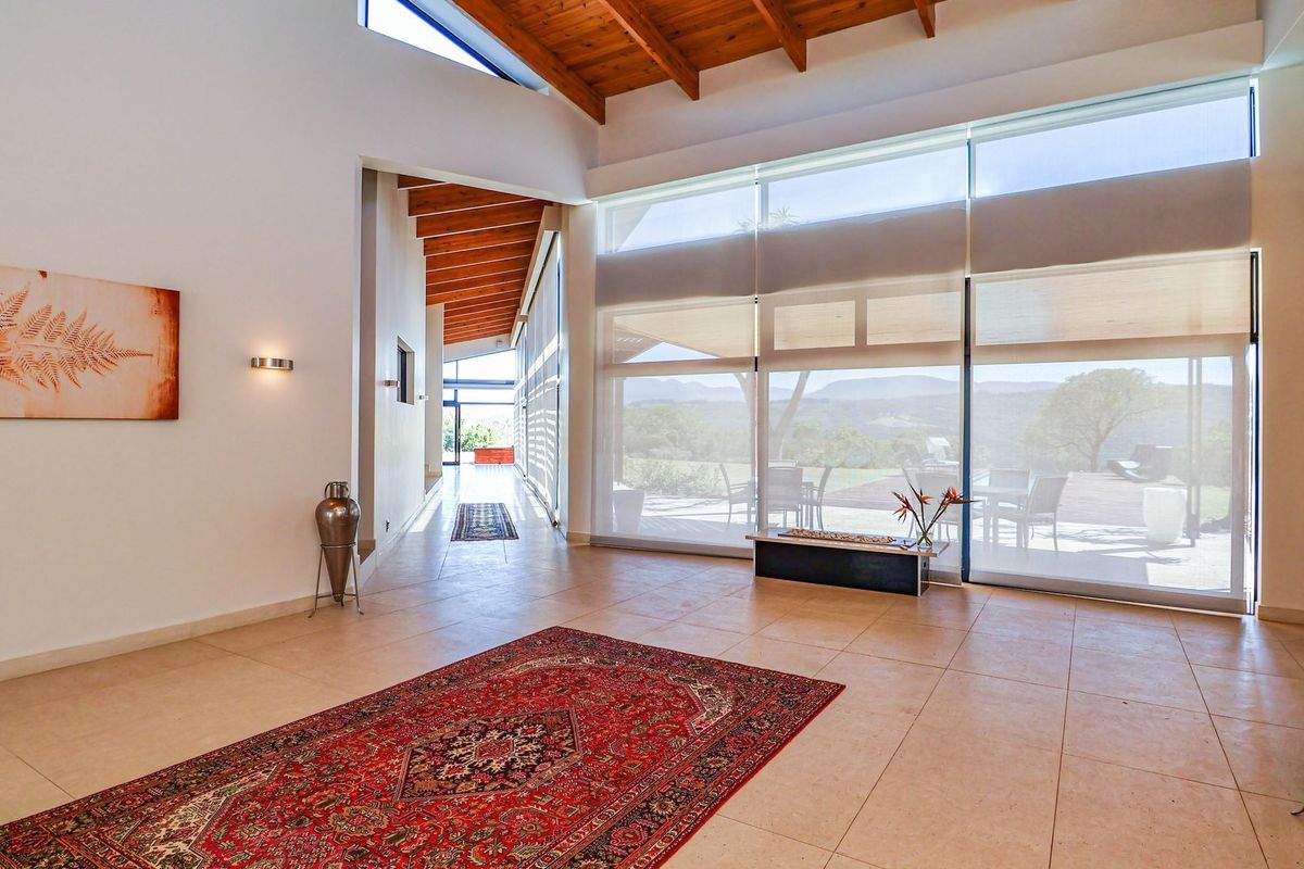Spacious living area featuring high exposed timber beam ceilings, large format floor tiles, and expansive floor-to-ceiling windows with scenic landscape views.