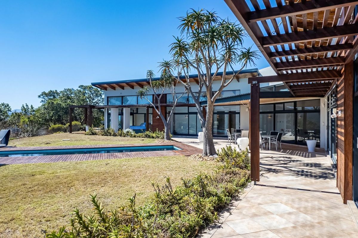 A modern farm-style rear exterior featuring a swimming pool, timber decking, a covered tiled patio with pergola, and expansive glass sliding doors.