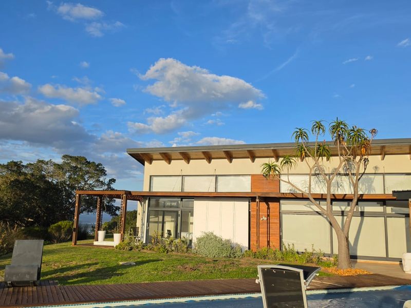 A modern rear exterior view of the farm property featuring a swimming pool, wooden decking, timber pergola, and expansive glass sliding doors.