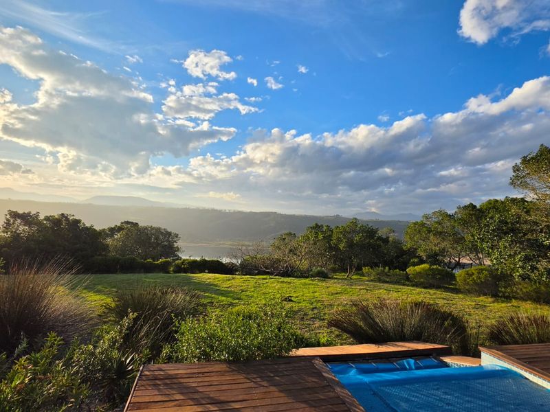 A scenic landscape view overlooking a lush green farm garden with a swimming pool and timber decking in the foreground.