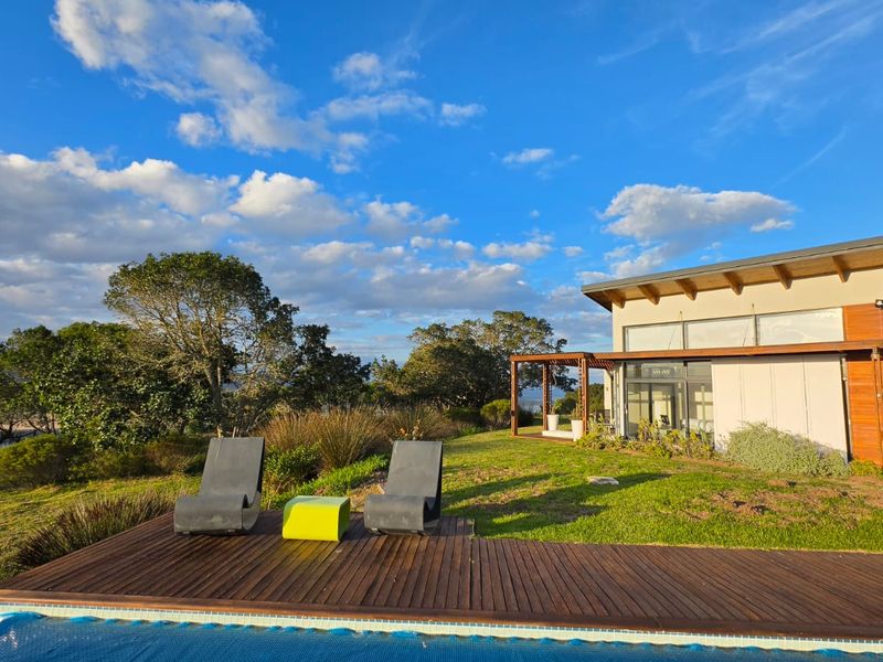 A well-maintained outdoor pool area featuring timber decking, a pergola, and views of the surrounding landscape, adjacent to the main residence.