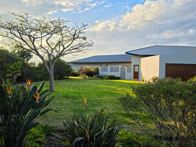 A well-maintained rear exterior view of the farm property featuring a spacious lawn, landscaped garden, and modern building structure with a metal roof.