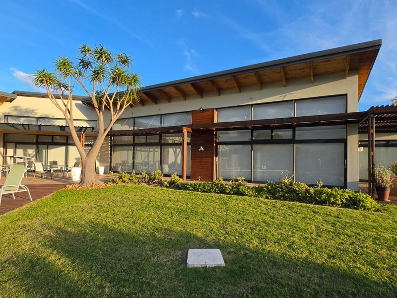 Modern rear facade featuring extensive timber decking, large glass sliding doors, and a timber pergola overlooking a well-maintained lawn and swimming pool area.