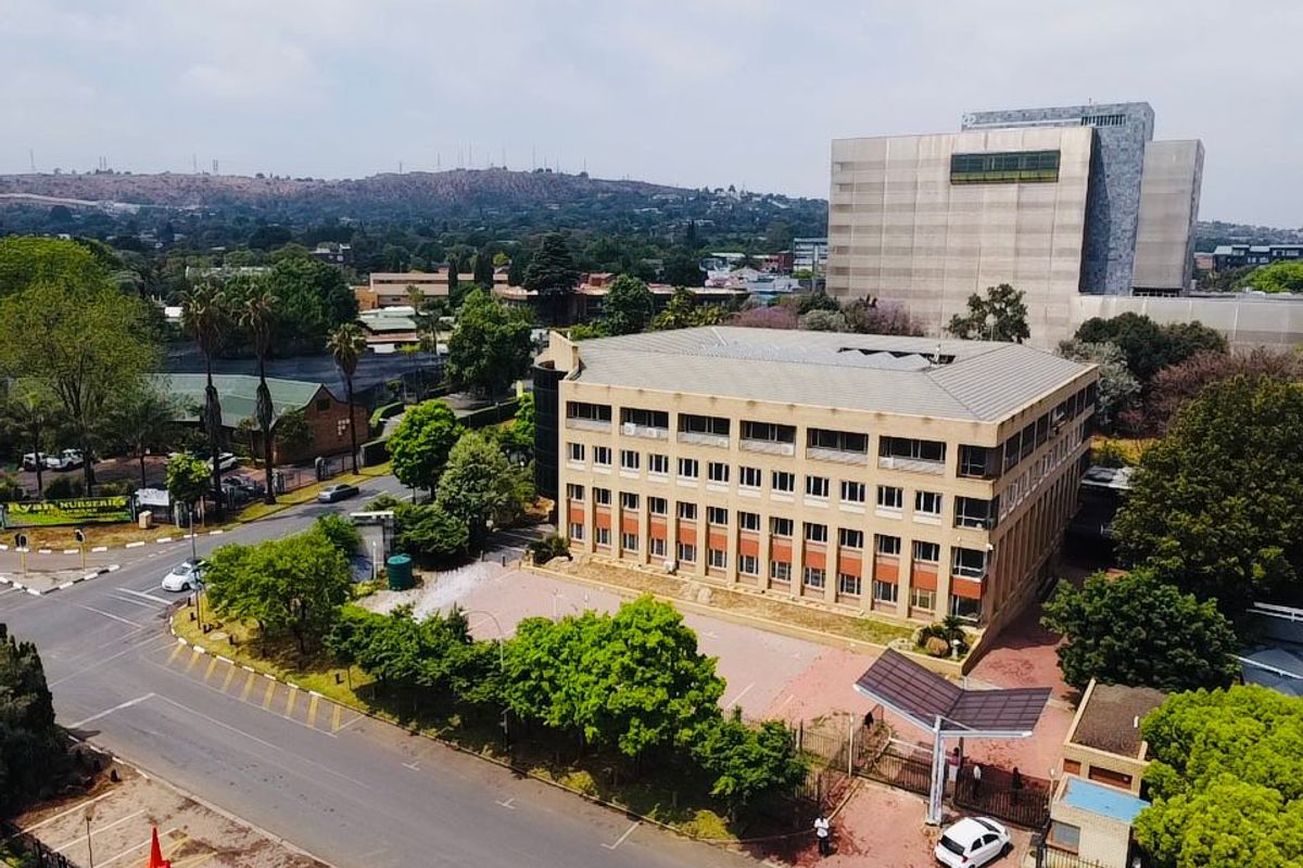 Aerial view of a multi-story commercial office building featuring a paved parking area, secure gated entrance, and surrounding landscaped grounds.