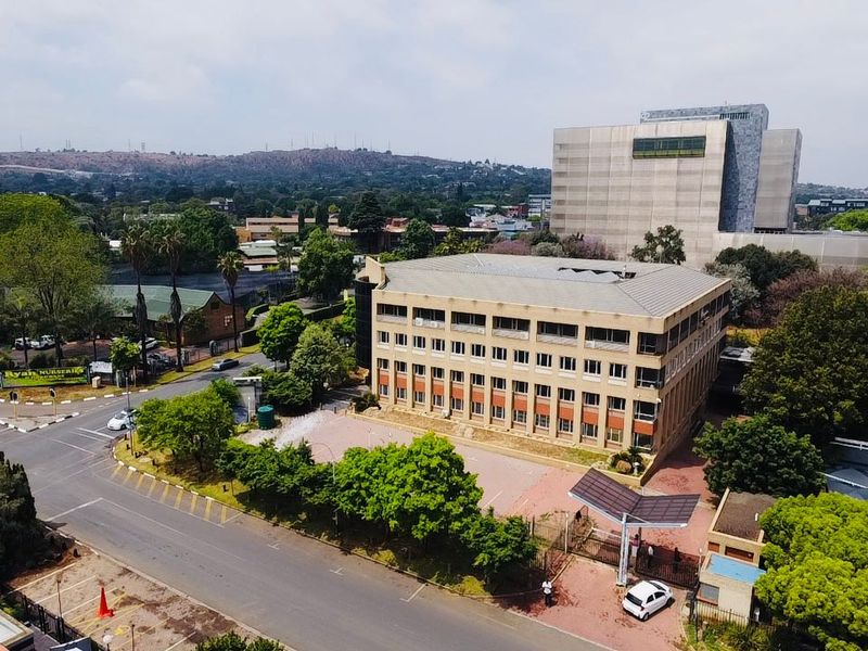 Aerial view of a multi-story commercial office building featuring a paved parking area, secure gated entrance, and surrounding landscaped grounds.