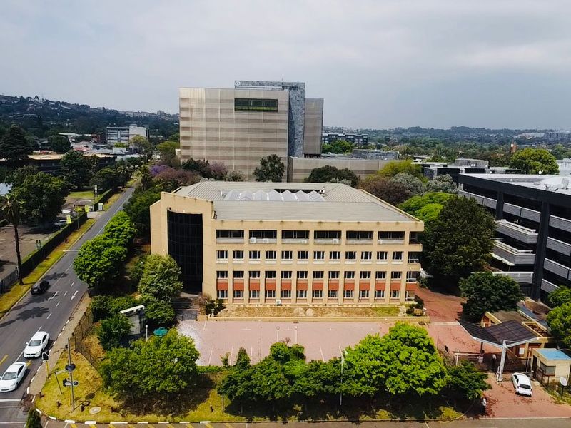 Aerial view of a multi-story commercial office building featuring a paved parking area and surrounding landscaped grounds in an urban setting.