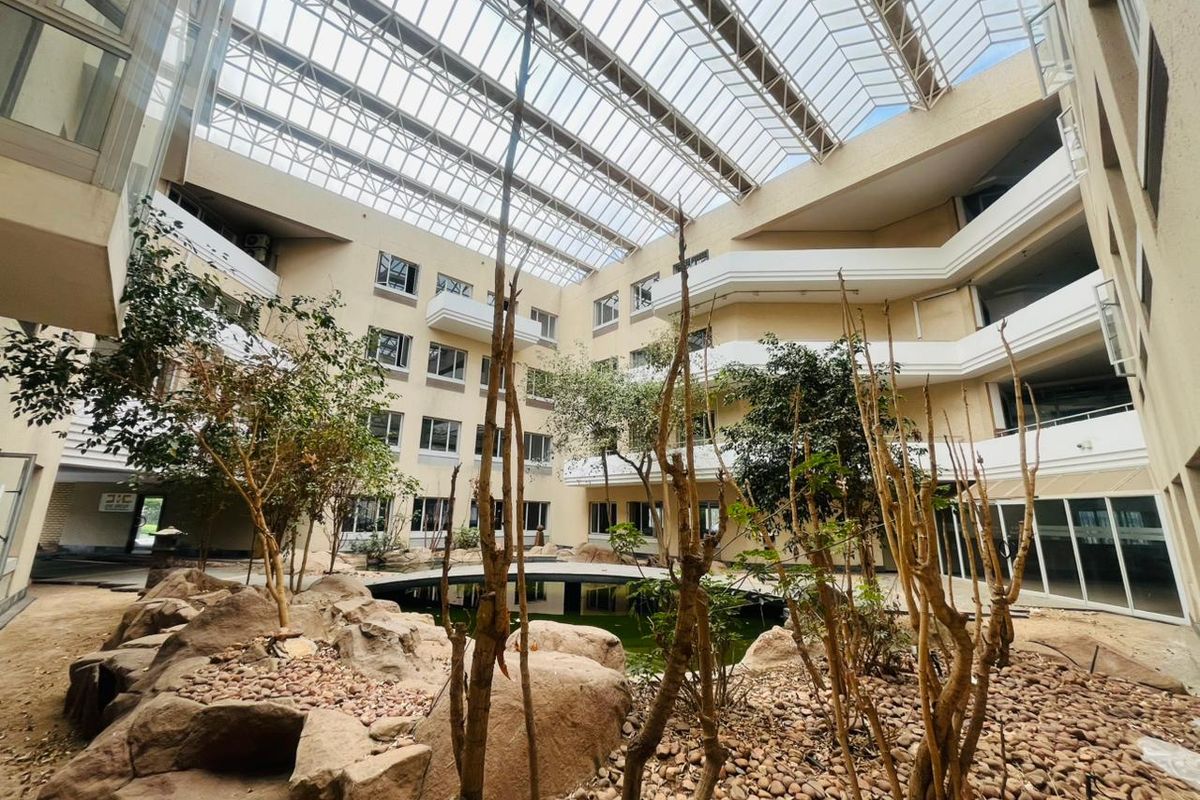 A large commercial atrium featuring a central water feature, rock garden, and multi-level balconies under a expansive glass skylight roof.