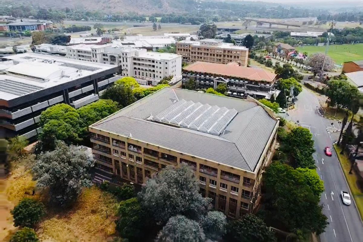 Aerial view of a multi-story commercial office building featuring a large central skylight and surrounding landscaped grounds in a business park setting.