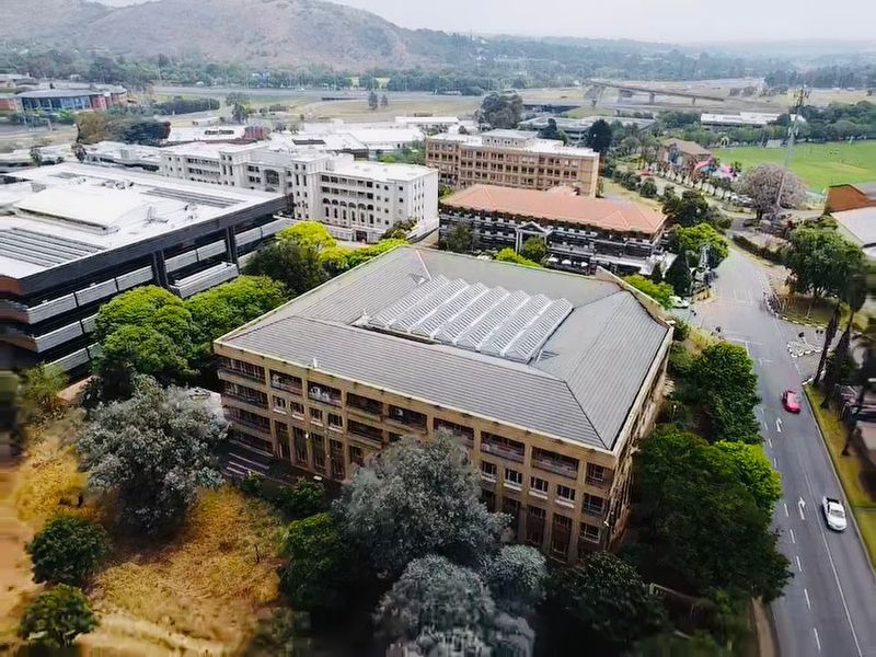 Aerial view of a multi-story commercial office building featuring a large central skylight and surrounding landscaped grounds in a business park setting.