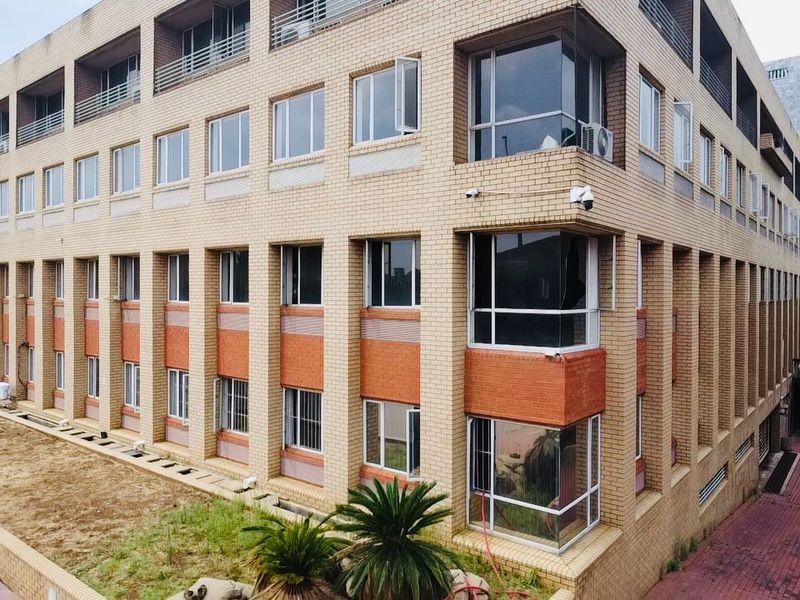 Multi-story commercial building featuring a brick facade, multiple windows, and integrated security cameras, with a paved driveway and surrounding landscaped area.