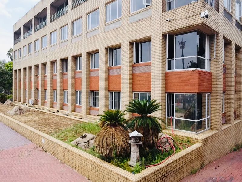 Exterior view of a multi-story commercial brick building featuring large windows, security cameras, and a landscaped retaining wall area.