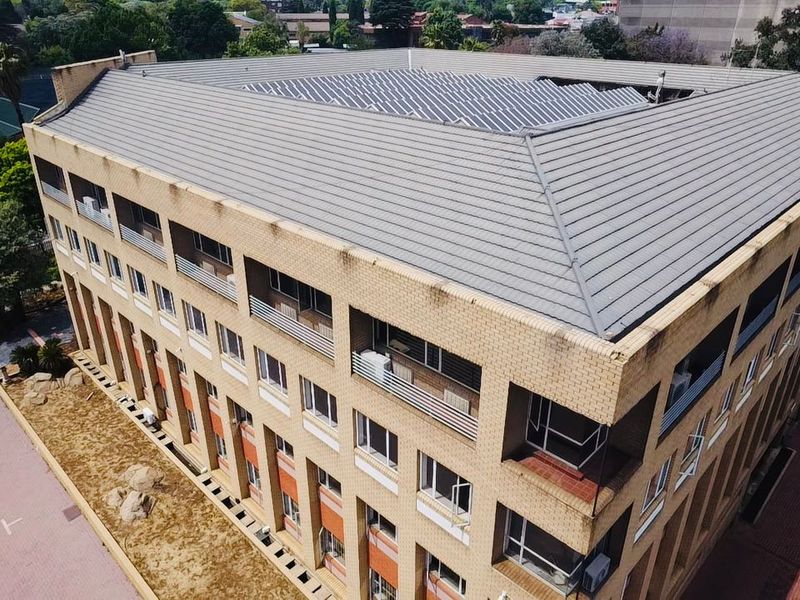 Aerial view of a multi-story commercial building featuring a tiled roof with integrated solar panels and a brick facade with multiple balconies.