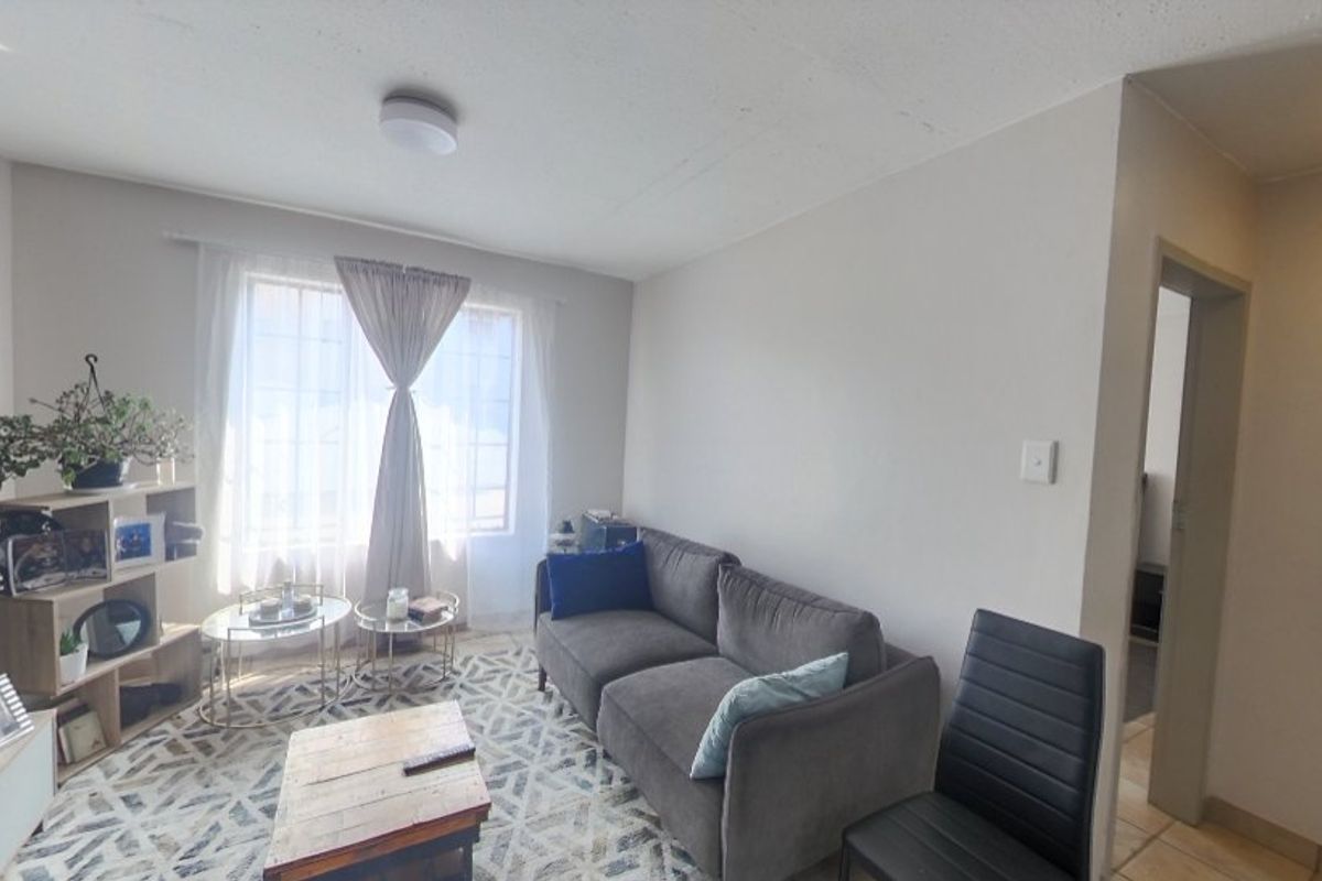 A bright living room featuring neutral walls, a large window with natural light, and a functional layout suitable for comfortable seating.
