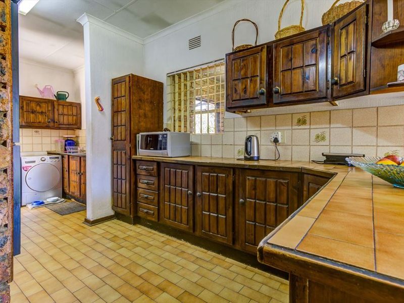 A functional kitchen featuring traditional wooden cabinetry, tiled countertops, and a distinct exposed brick feature wall, offering a classic, dated aesthetic.