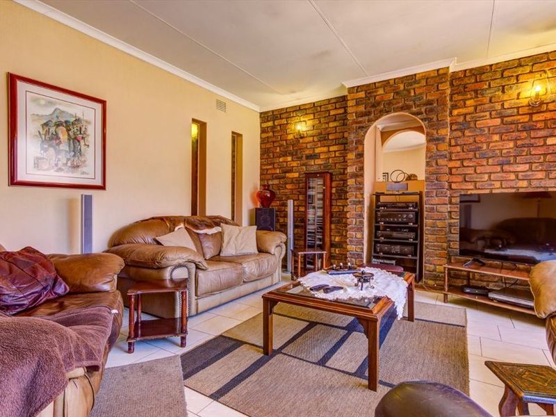 A cozy living room featuring an exposed brick accent wall, arched architectural detail, and neutral tiled flooring.