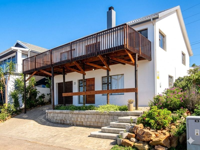 Front elevation of a two-story house featuring a prominent raised timber deck, paved driveway, concrete retaining wall, and established garden landscaping.