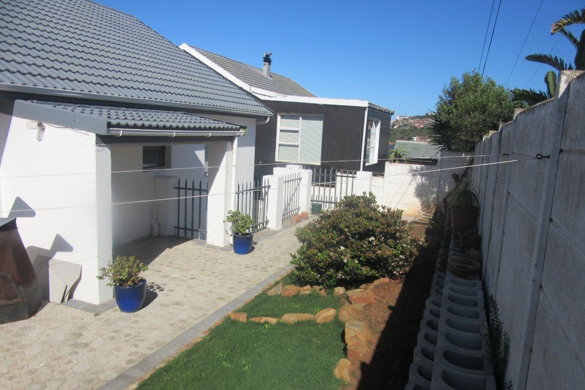 A rear exterior view featuring a paved patio area, a small lawn, and a secure boundary wall with metal gate access.