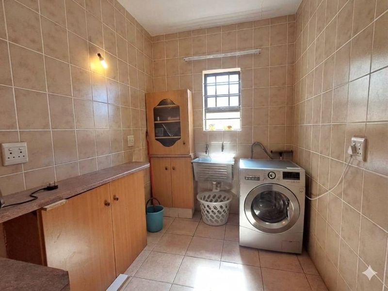 Functional laundry room featuring full-height wall tiling, built-in cabinetry with laminate countertops, and a stainless steel utility sink.