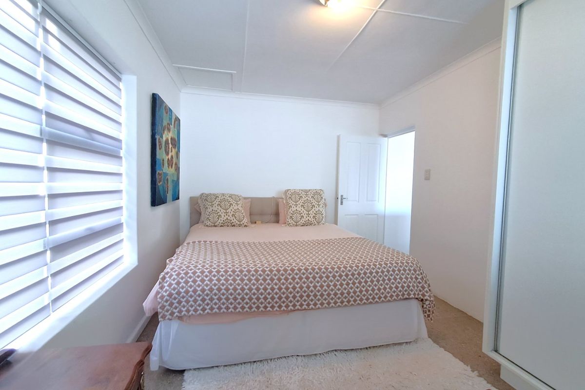 A functional bedroom featuring a built-in wardrobe, neutral wall finishes, and window blinds, providing a clean and simple living space.