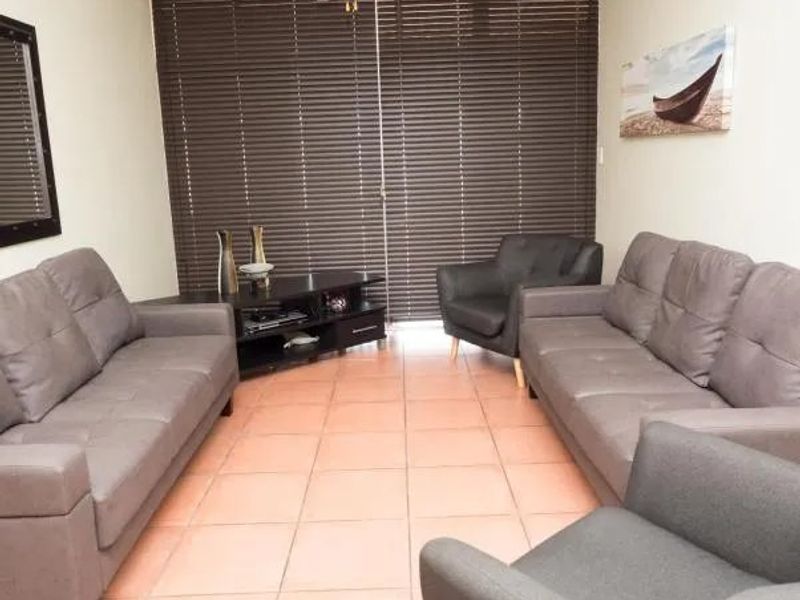 A living room featuring tiled flooring and dark venetian blinds covering the window area.