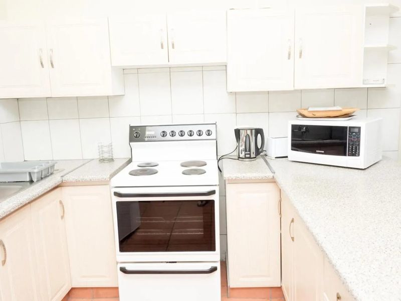 A functional kitchen featuring white cabinetry, laminate countertops, a tiled backsplash, and a freestanding electric stove.