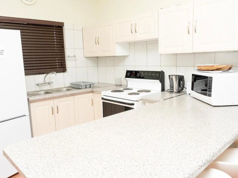 A functional kitchen featuring light-toned built-in cabinetry, laminate countertops, a double basin sink, and a freestanding electric stove with a tiled backsplash.