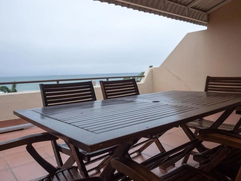 A covered balcony featuring tiled flooring and a metal railing, offering an open view of the ocean.