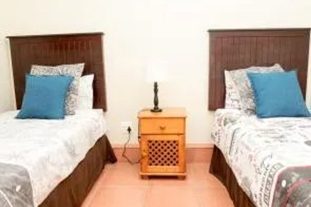 A bedroom featuring tiled flooring and a central bedside table between two bed spaces.