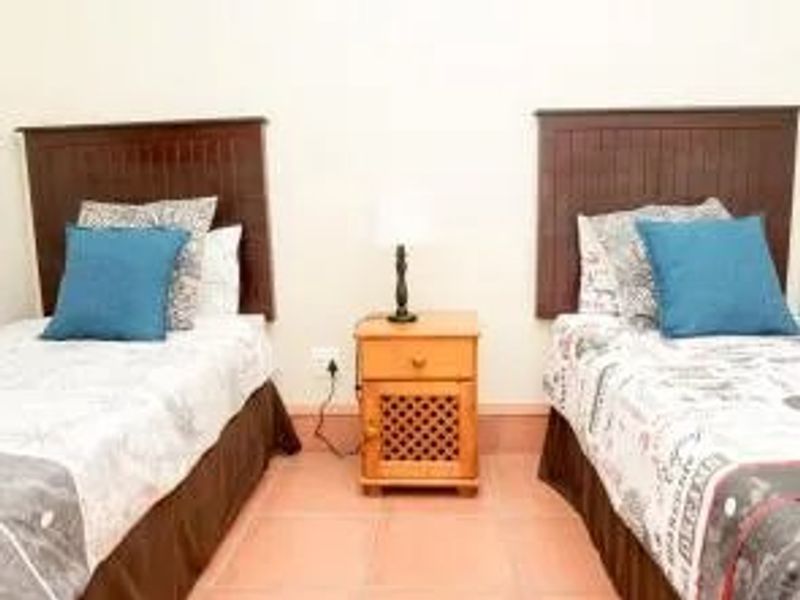 A bedroom featuring tiled flooring and a central bedside table between two bed spaces.