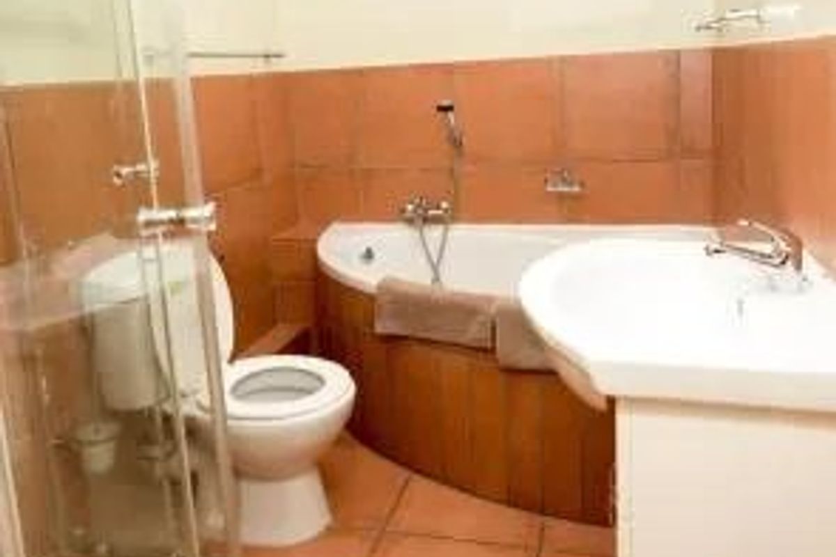 A functional bathroom featuring a corner bathtub, glass shower enclosure, pedestal washbasin, and toilet with dated ceramic wall and floor tiling.