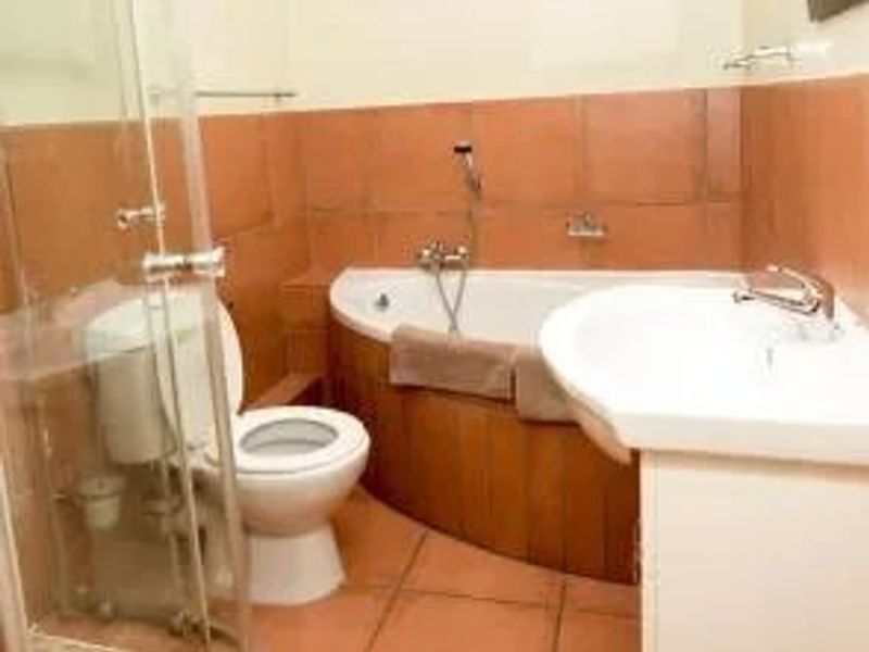A functional bathroom featuring a corner bathtub, glass shower enclosure, pedestal washbasin, and toilet with dated ceramic wall and floor tiling.