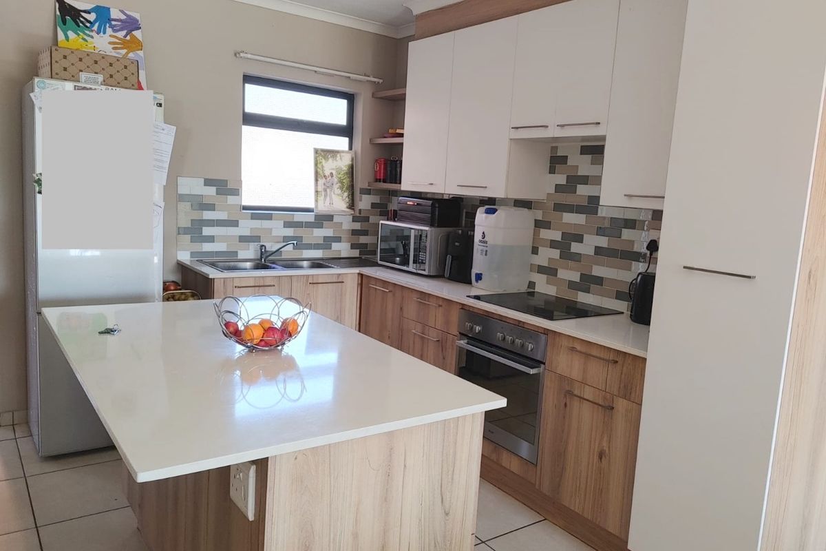 Modern kitchen featuring a central island, stone countertops, built-in oven with electric hob, and ample storage cabinetry with a tiled backsplash.