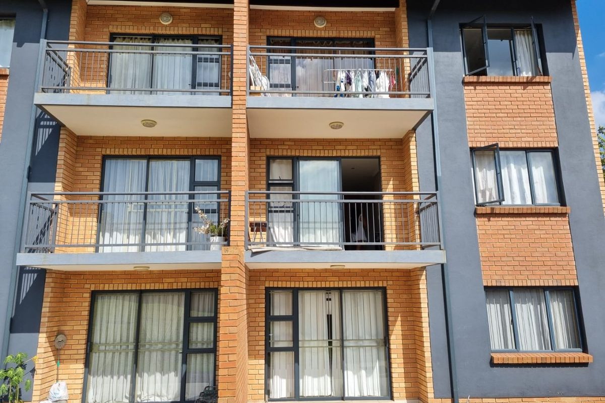 A multi-story apartment building facade featuring face-brick construction, private balconies with metal railings, and large sliding glass doors for each unit.