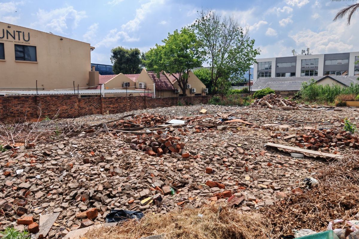Vacant residential land plot featuring a brick boundary wall with electric fencing, currently covered in construction debris and rubble.