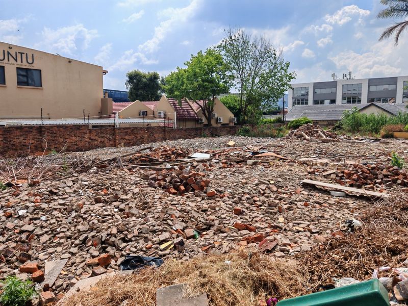 Vacant residential land plot featuring a brick boundary wall with electric fencing, currently covered in construction debris and rubble.