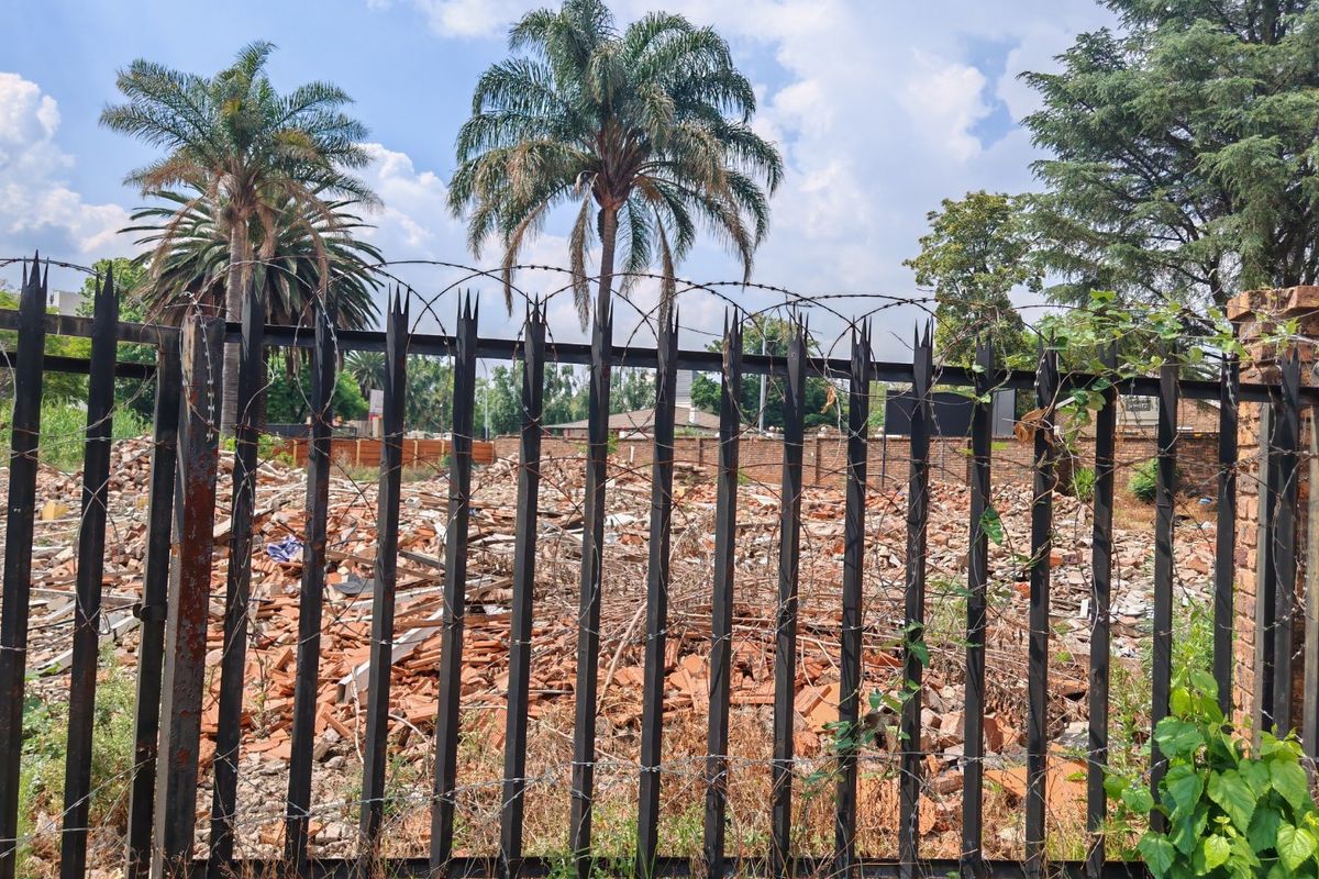 Vacant residential land featuring a metal security fence and significant demolition rubble on site, ready for clearing and new development.