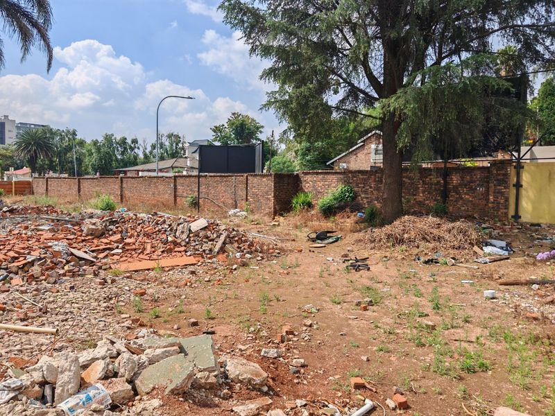 Vacant residential land featuring a brick boundary wall, mature tree, and significant site debris requiring clearing for future development.