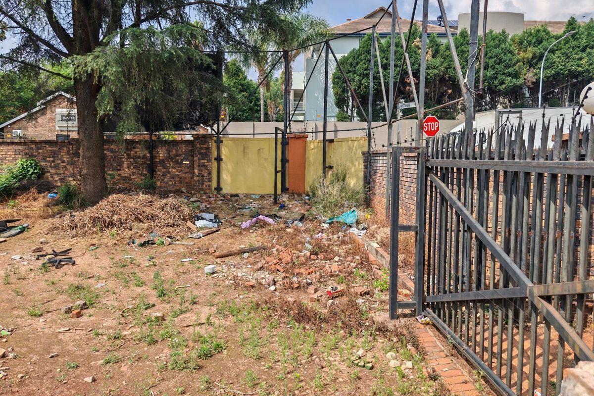 Vacant residential land featuring a metal security gate, brick boundary walls, and an existing large billboard structure on site.