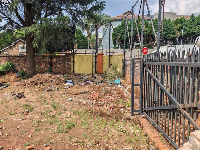 Vacant residential land featuring a metal security gate, brick boundary walls, and an existing large billboard structure on site.