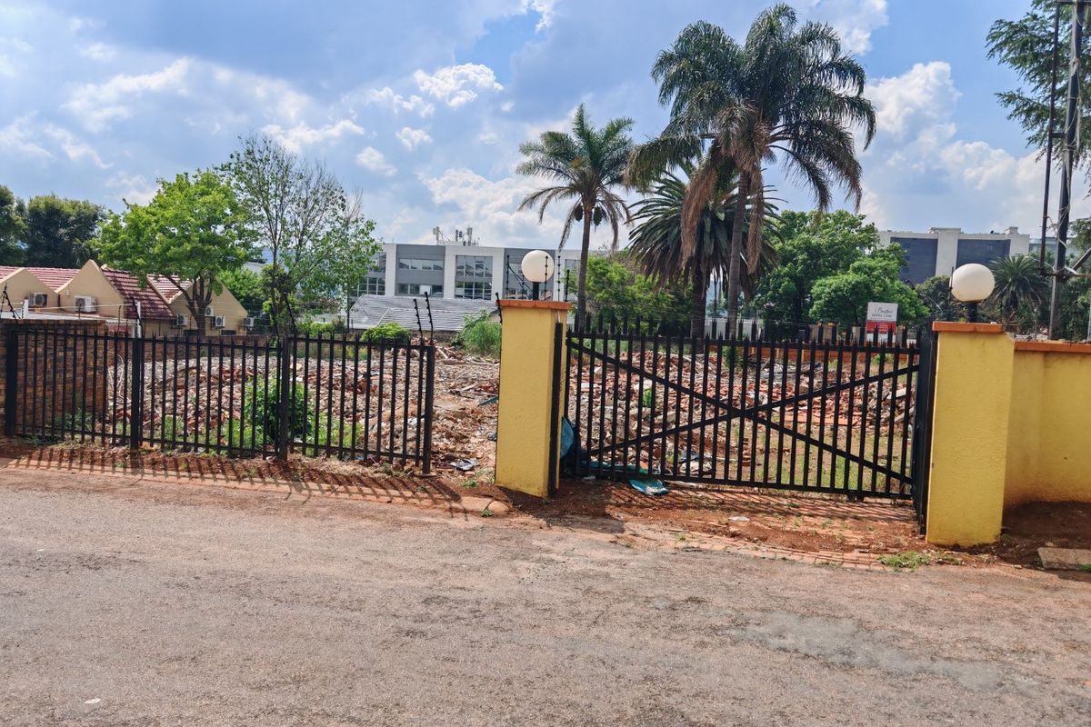 Vacant residential land featuring perimeter metal fencing, gated entrance, and electric security fencing, currently containing demolition debris from previous structures.